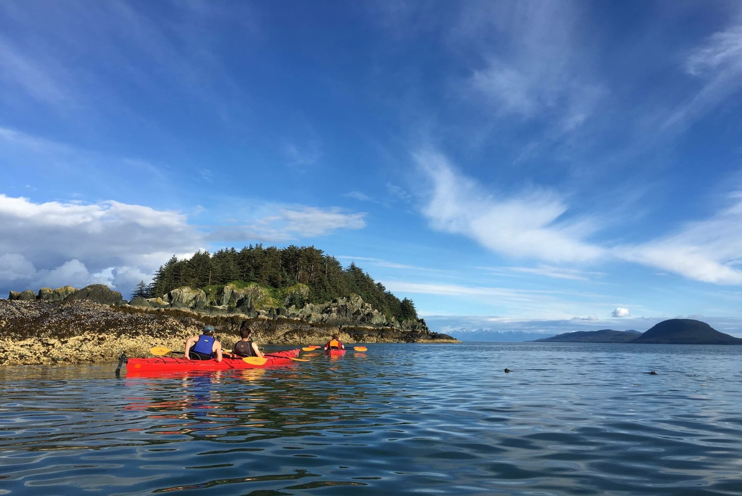 Sea kayakers paddling near coastal island under blue sky