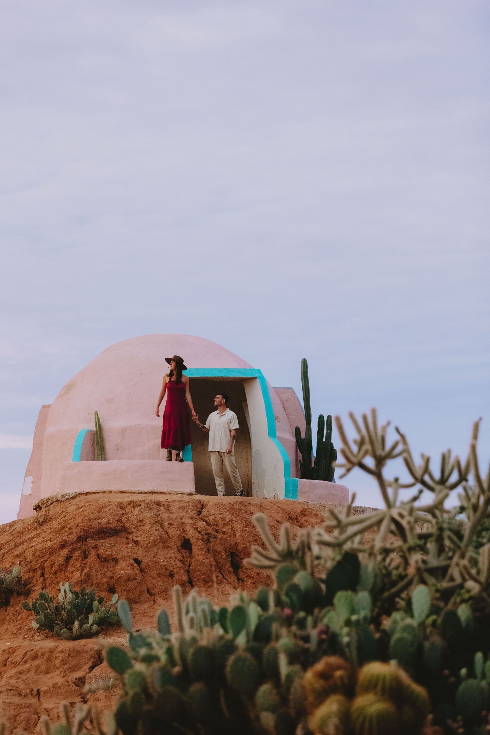 Couple on adobe dome overlooking cactus-studded desert hill