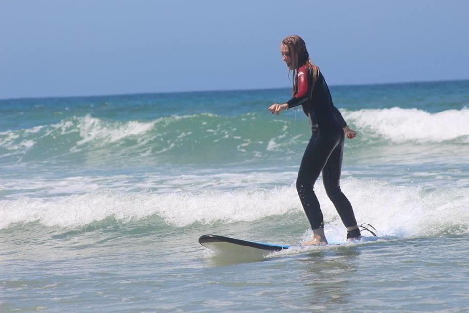 Surfer riding small ocean wave near sandy beach in wetsuit