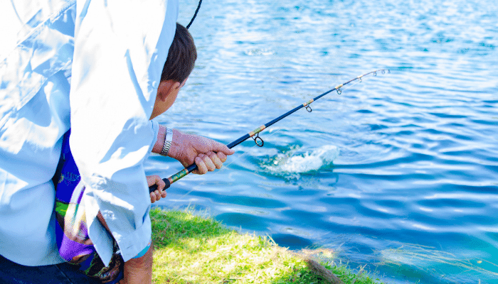 Angler casting line into calm lake from grassy shoreline