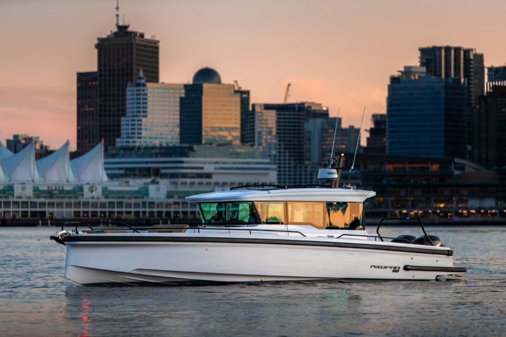 Motorboat cruising past city skyline at sunset on coastal waters