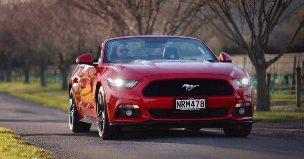 Red convertible Mustang driving on scenic country road