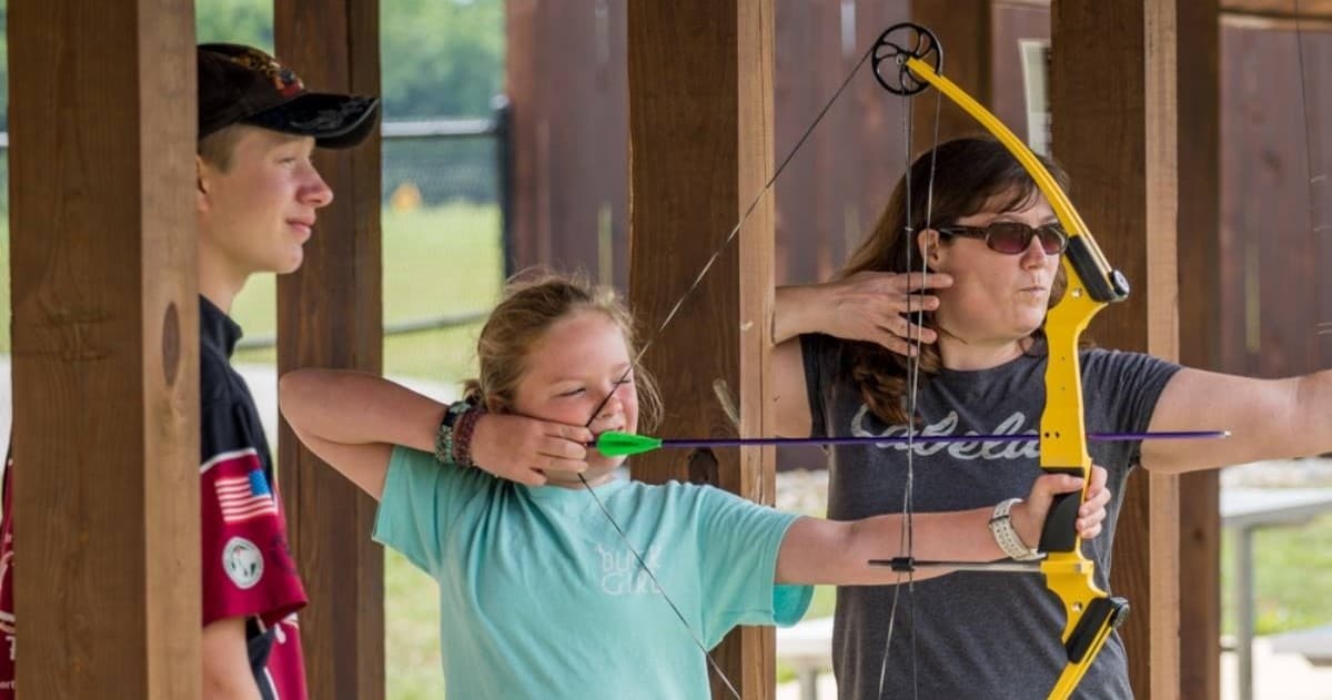 Teens practicing archery under covered outdoor instruction range