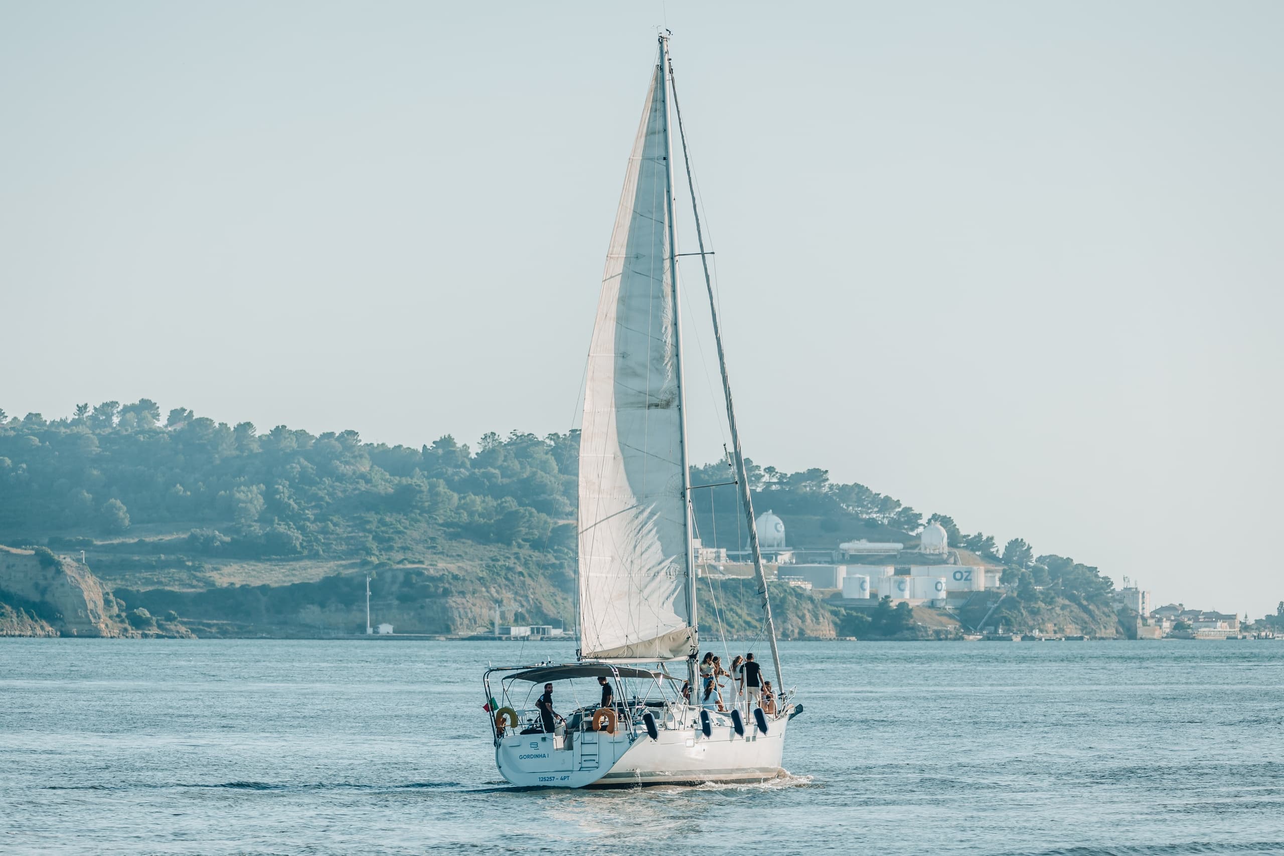 Ocean sailboat under full sail off coastal shoreline at sea