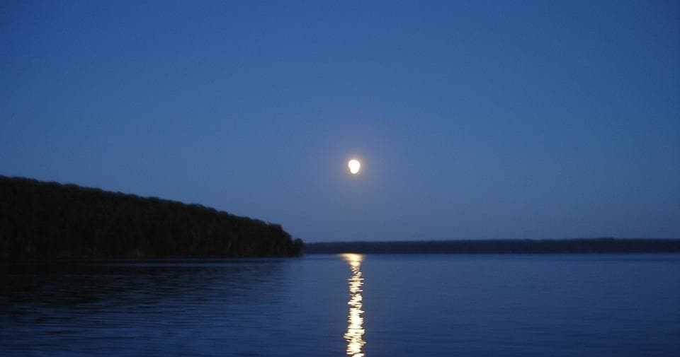 Full moon reflecting on calm lake at dusk, tranquil waterfront