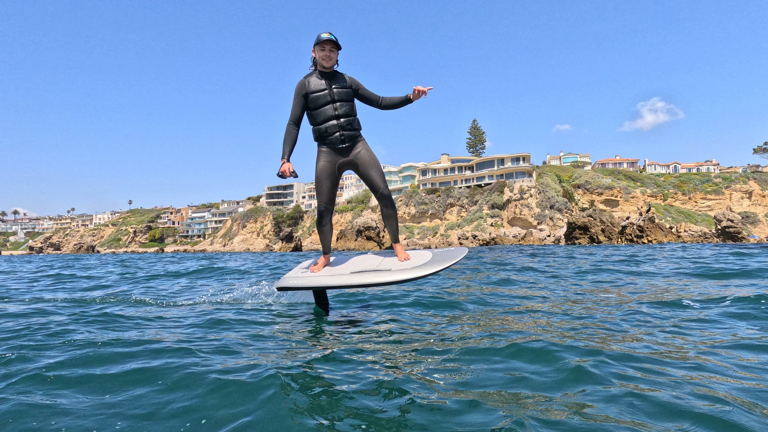 Foil surfer carving near rocky coastline on a sunny day