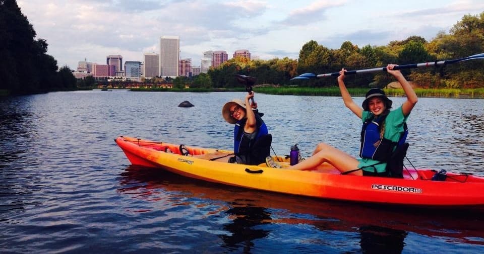 Two kayakers paddling on river with city skyline backdrop