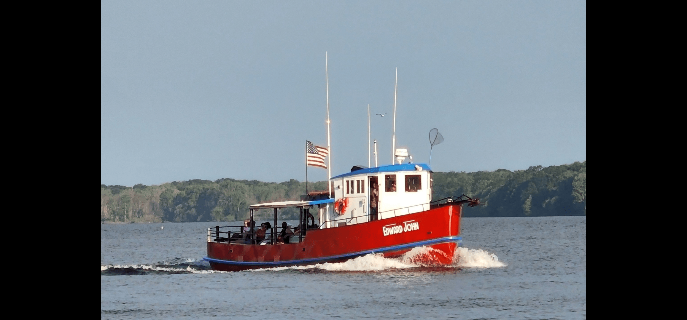 Red charter fishing boat cutting through lake waters, anglers aboard