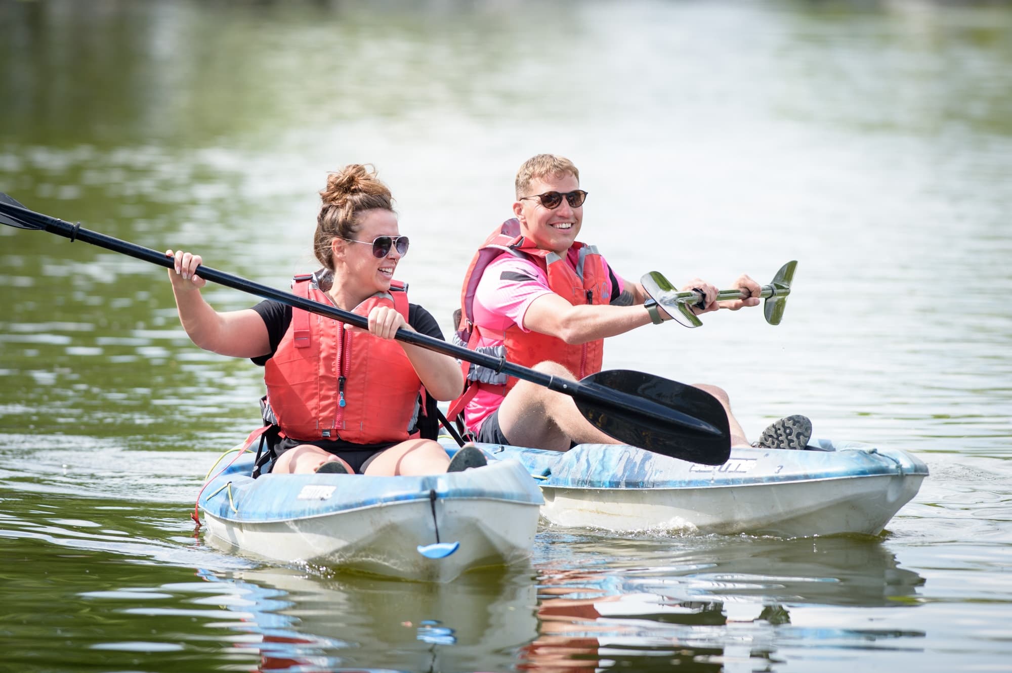 Two kayakers paddling tandem on calm river in life jackets