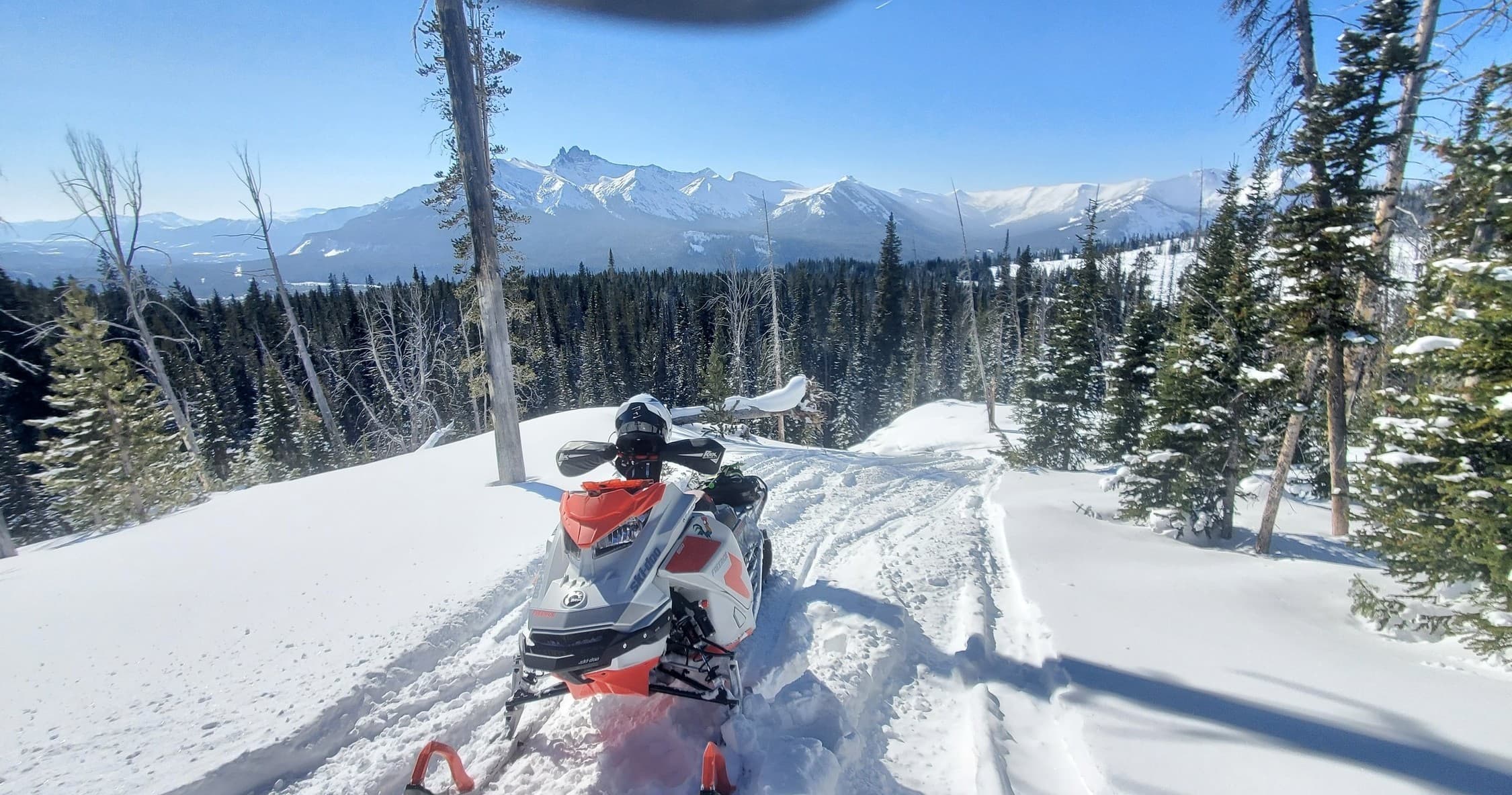 Snowmobiler riding ridge trail with panoramic Beartooth mountains