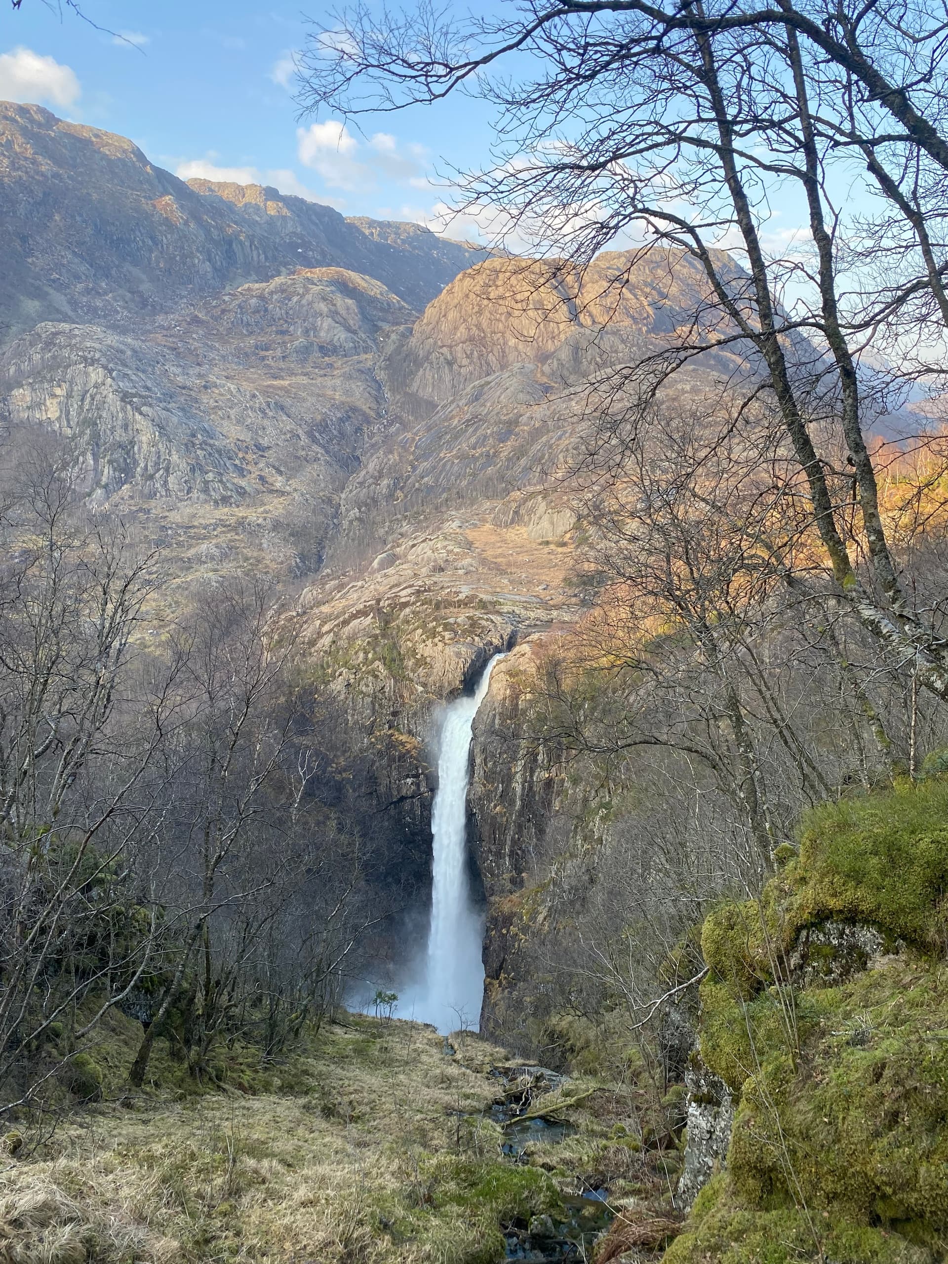 Hiker approaching tall mountain waterfall in rugged Norwegian valley