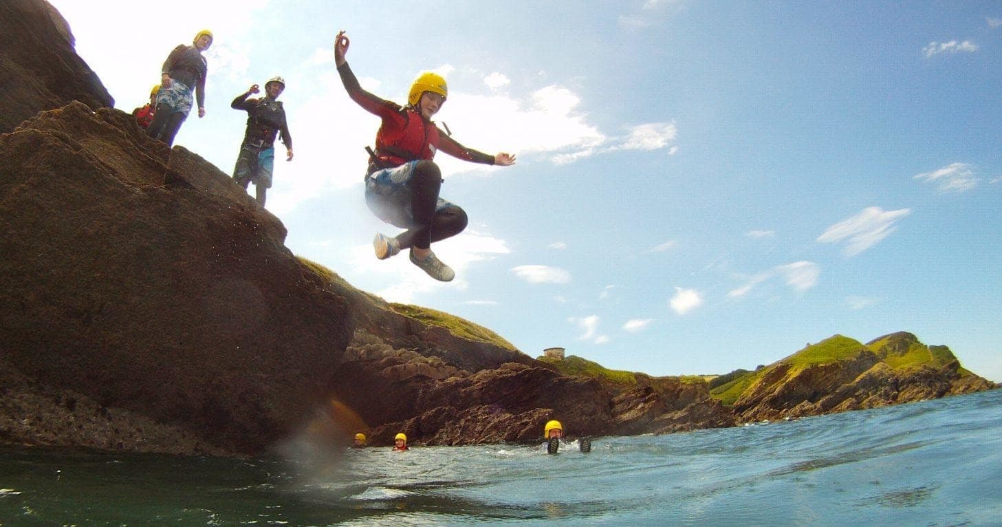 Group jumping from coastal rocks into blue sea near cliffs