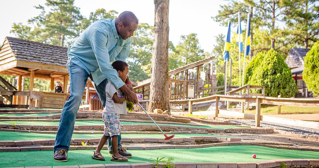 Father teaching child mini golf at outdoor family attraction