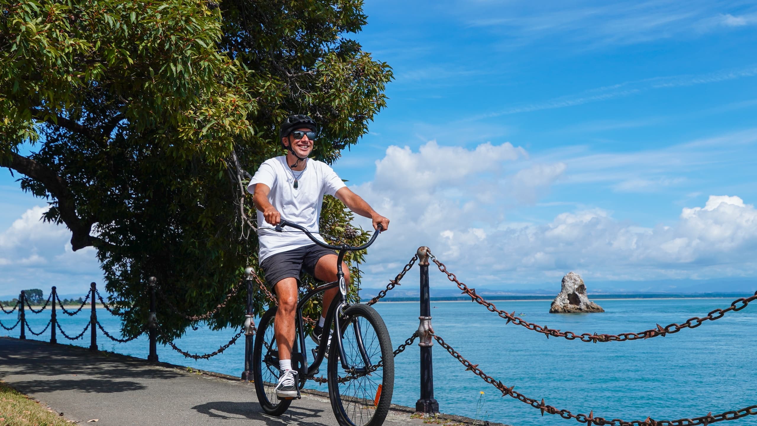 Cyclist standing by coastal railing admiring sea and rocky islands