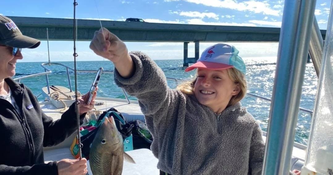 Young angler reeling in catch on family sportfishing trip near bridge