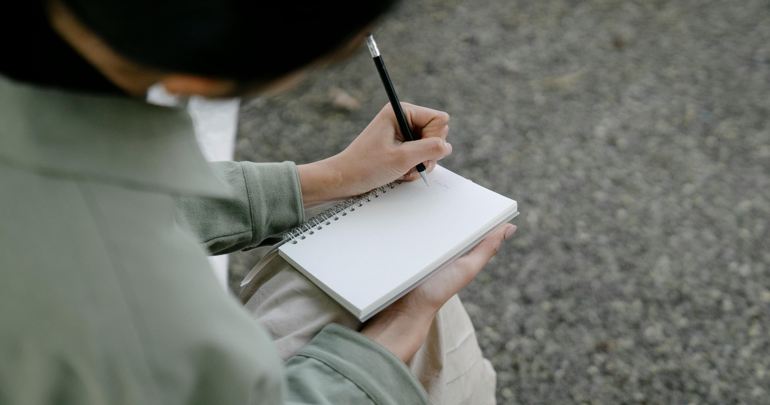 Person journaling outdoors on a gravel path with notebook