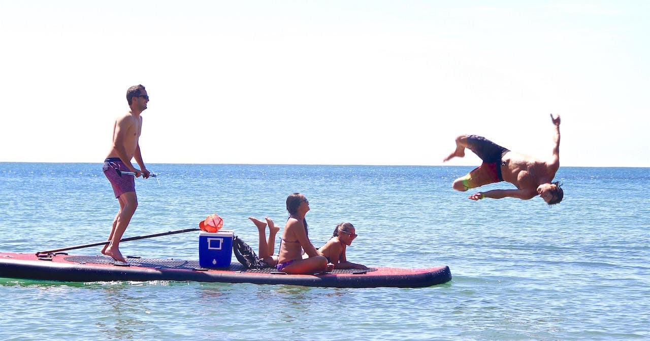 Friends diving off paddleboard into clear ocean near shore