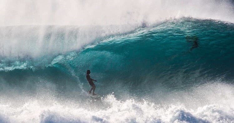 Surfer navigating a large turquoise breaking wave in ocean