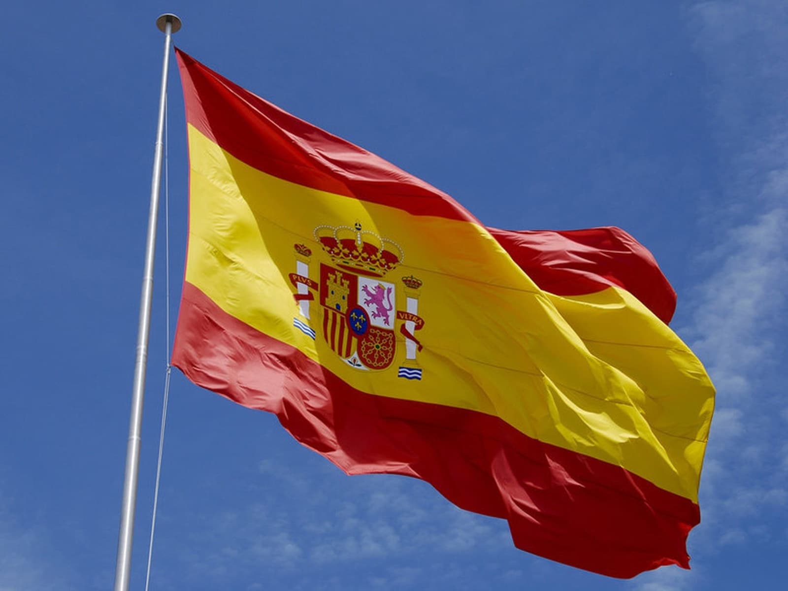 Spanish flag waving outdoors against blue sky at historic site