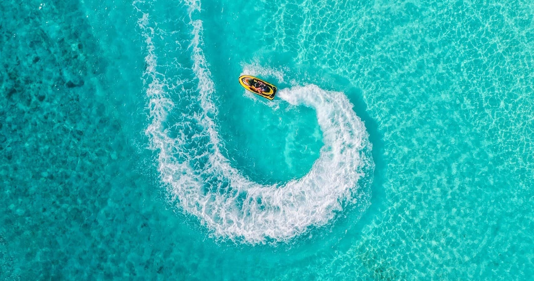 Aerial jet ski carving turquoise lagoon, dramatic swirl wake