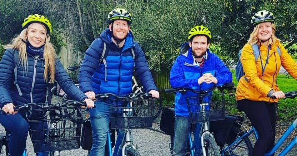 Four bikers smiling in helmets on a cool-weather vineyard ride