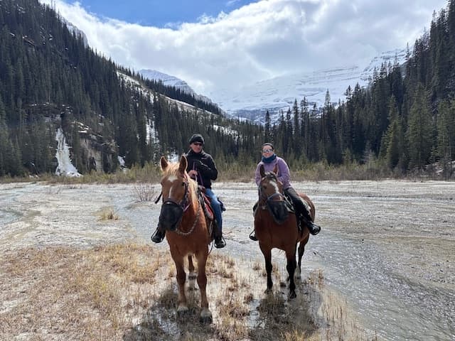 Two riders fording alpine stream on horseback in mountain valley