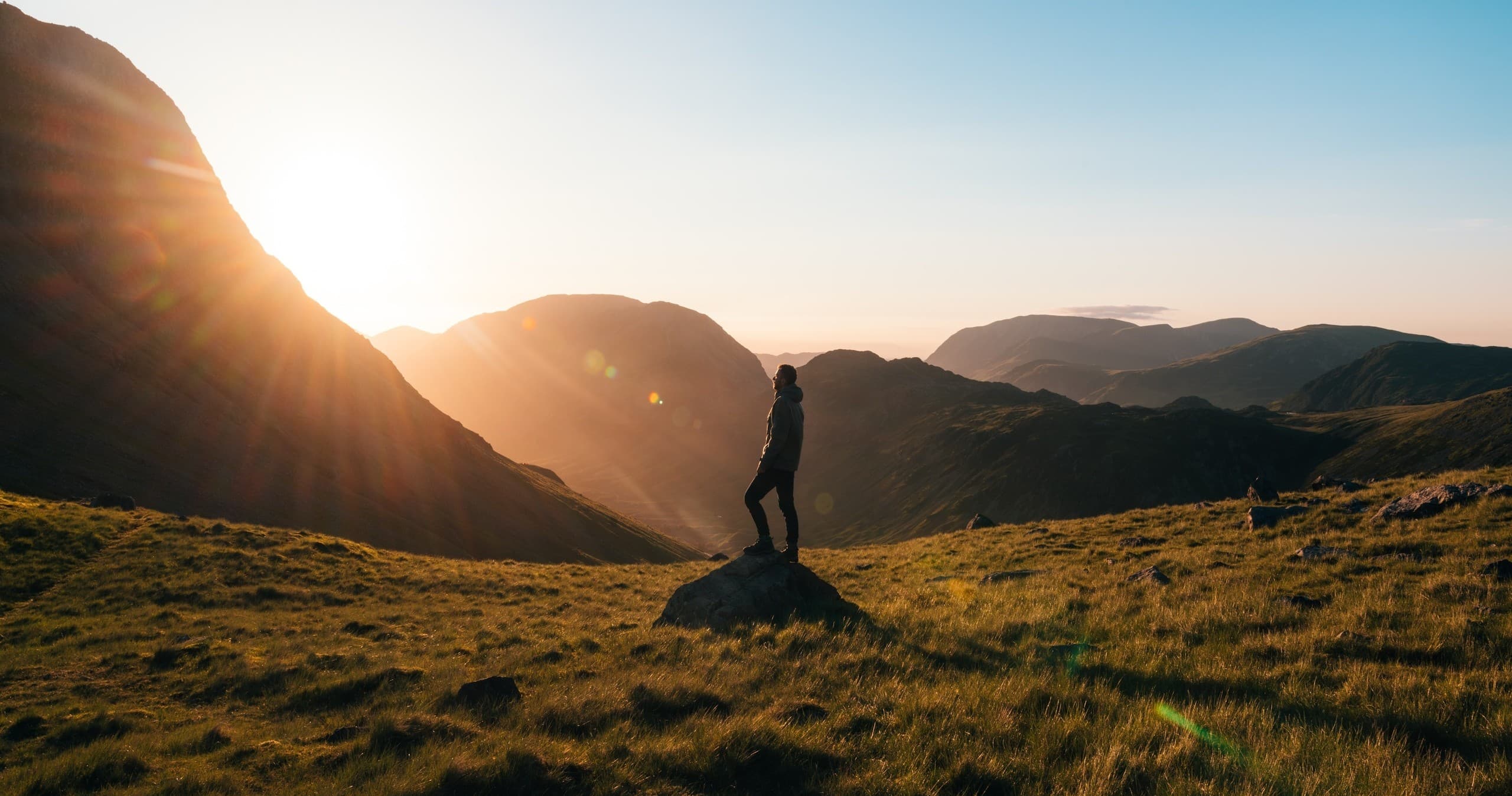 Hiker standing on grassy mountain ridge at sunrise