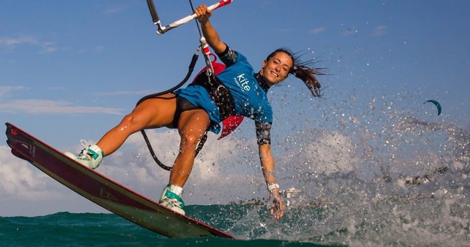Female kiteboarder carving wave with spray in tropical waters