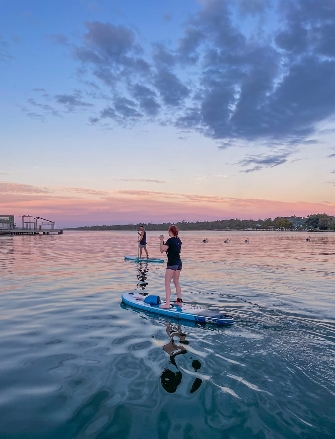 Paddleboarders at dusk on reflective water under colorful sky