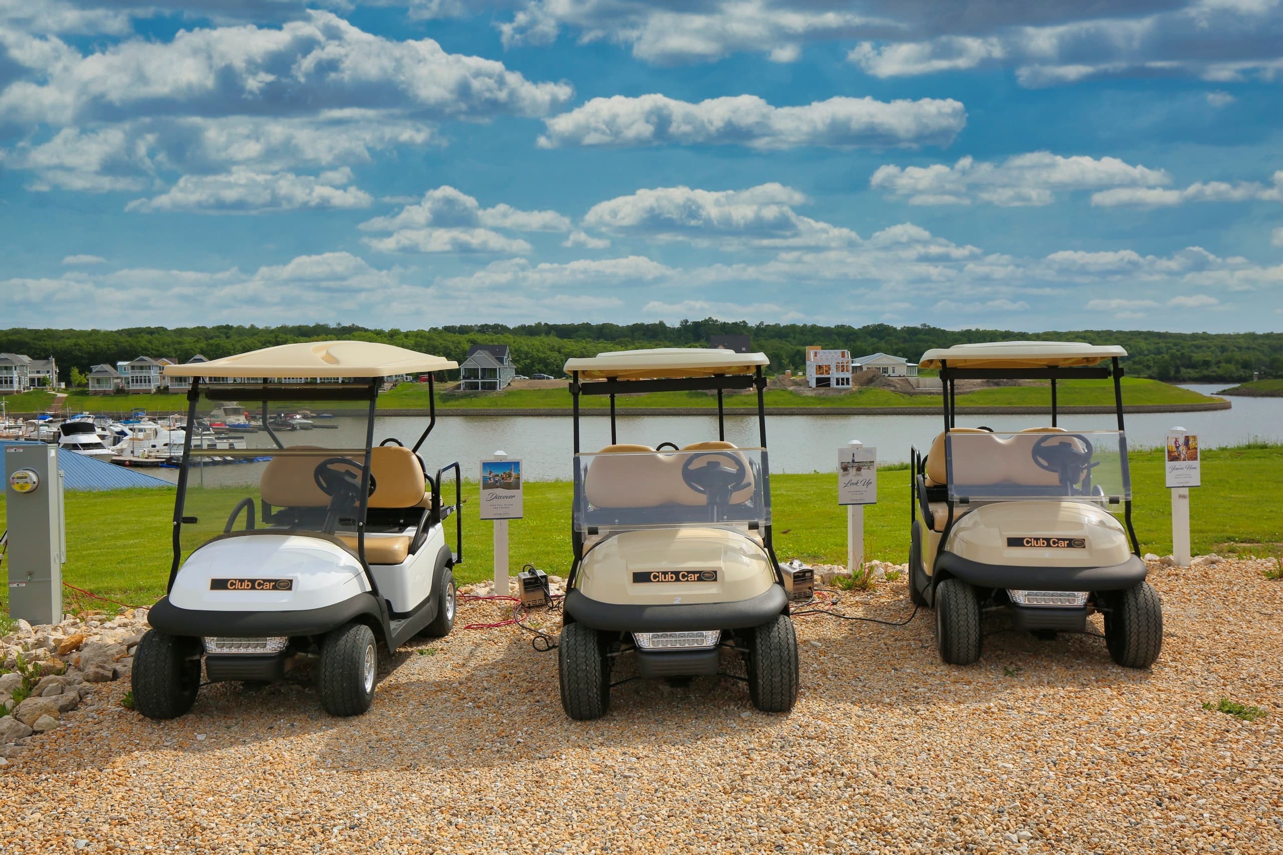 Golf carts parked by scenic harbor with cloudy blue sky