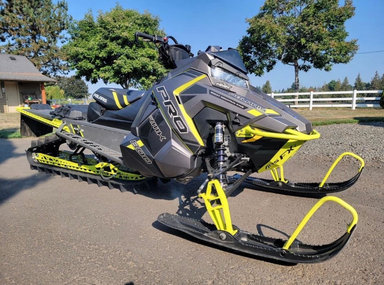 Yellow snowmobile parked on paved road near open pasture