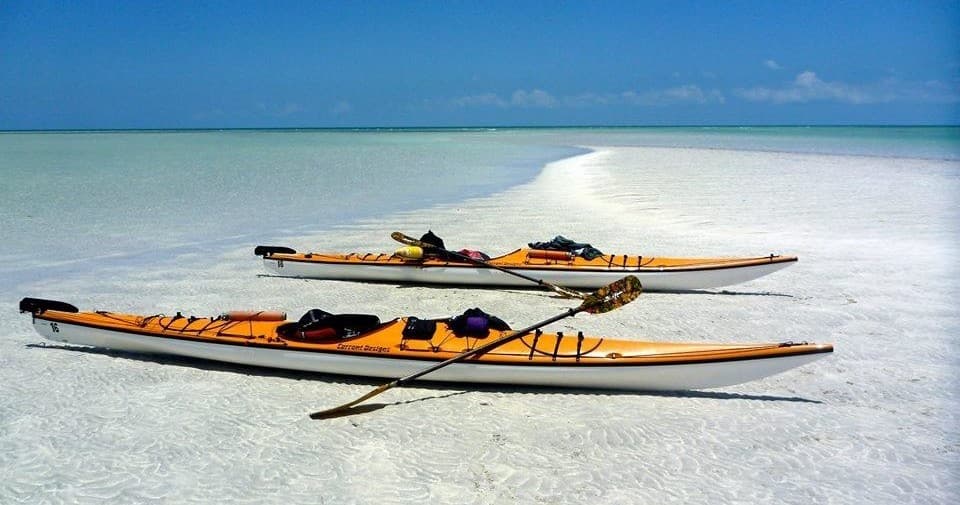 Sea kayaks resting on white sand flats in clear tropical bay