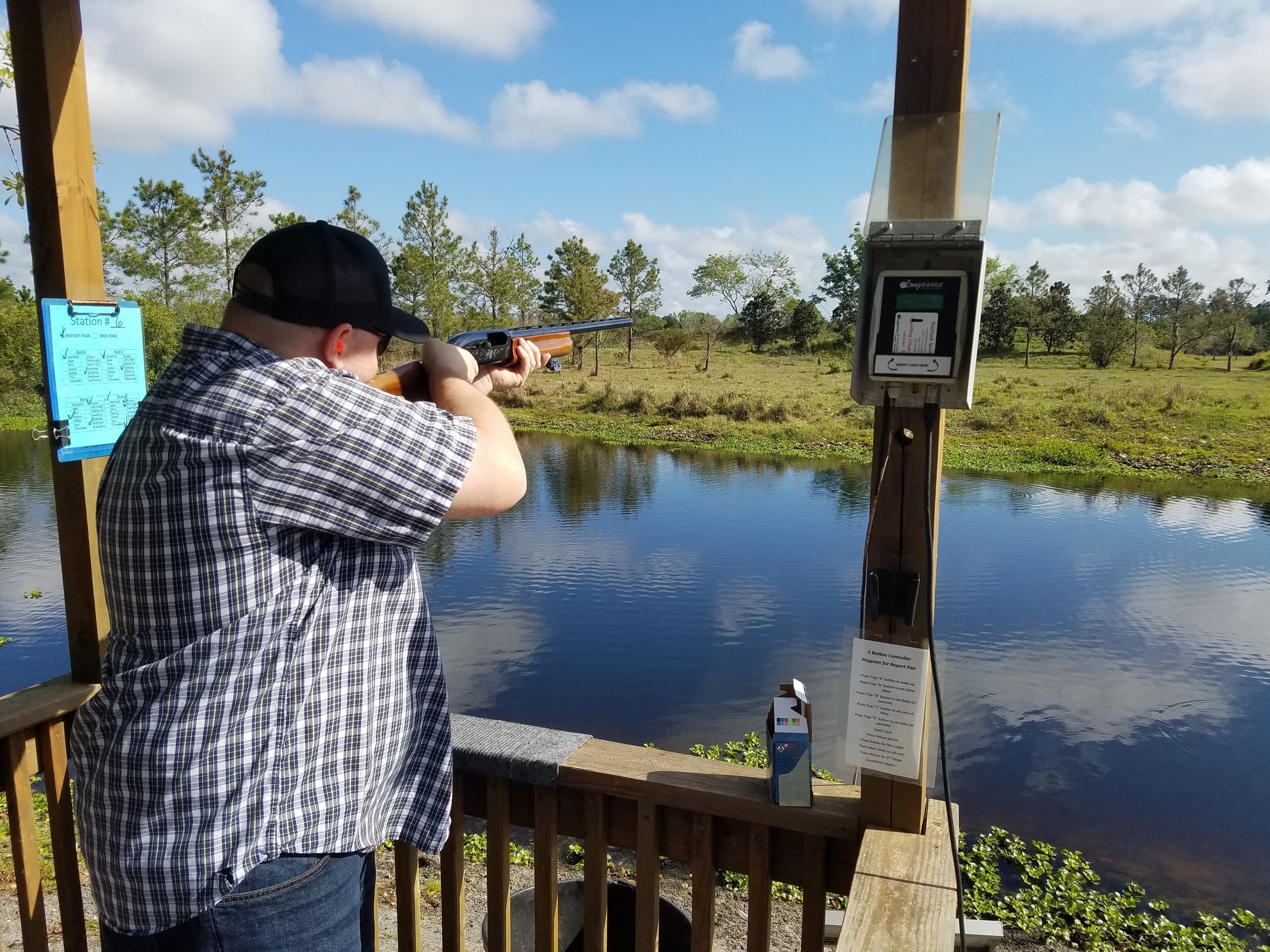 Shooter firing at outdoor lakeside range with scenic marsh