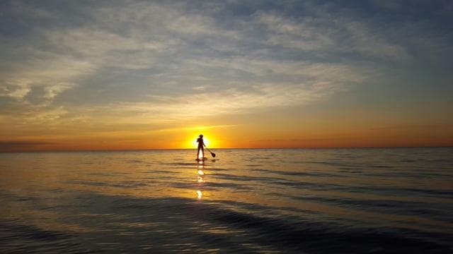 Paddleboarder silhouetted at sunset on calm open ocean