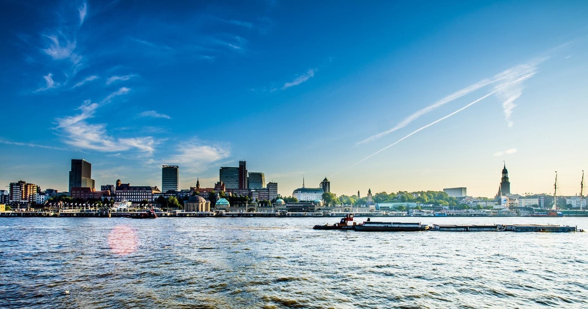 Harbor boat cruising past Hamburg skyline under blue sky