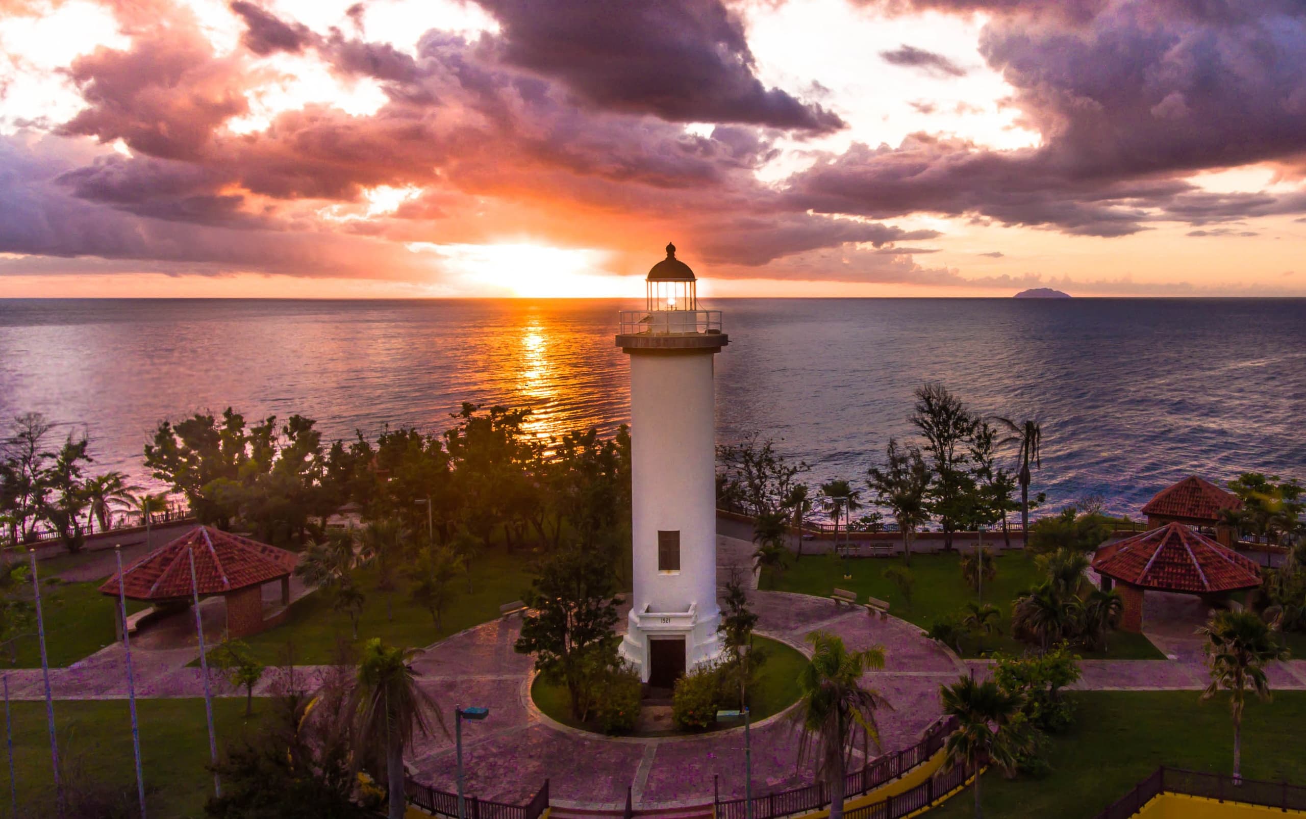 Coastal lighthouse at sunset overlooking ocean and palm gardens