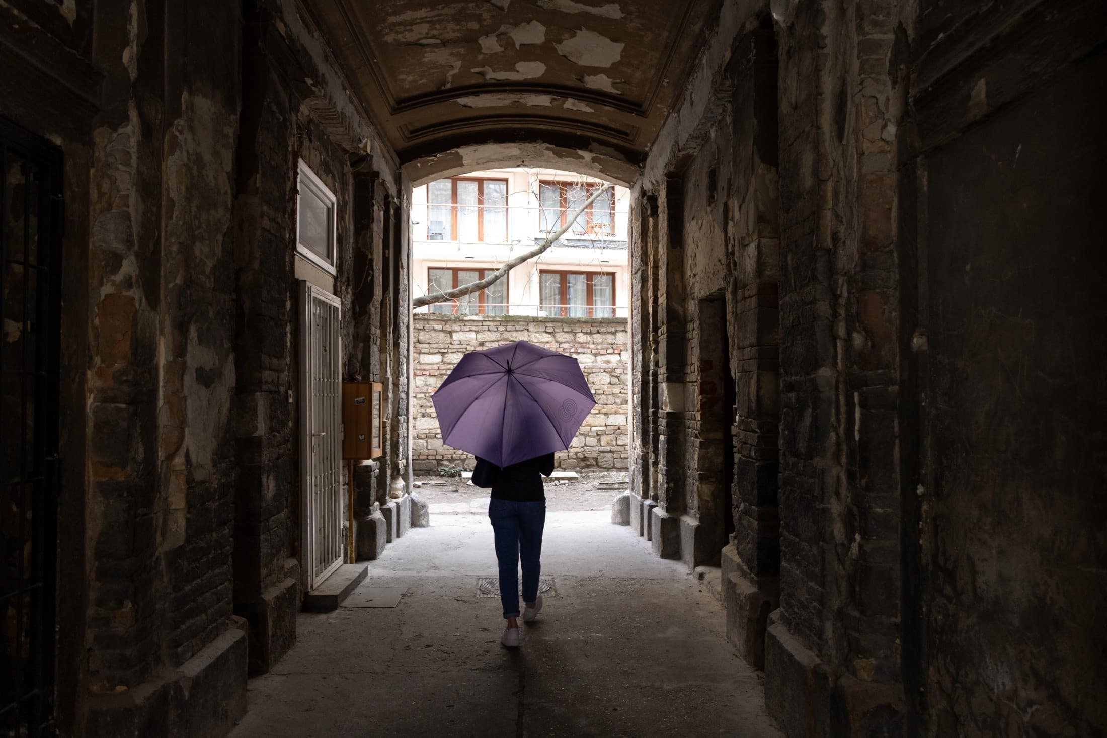 Person walking under purple umbrella through historic stone archway