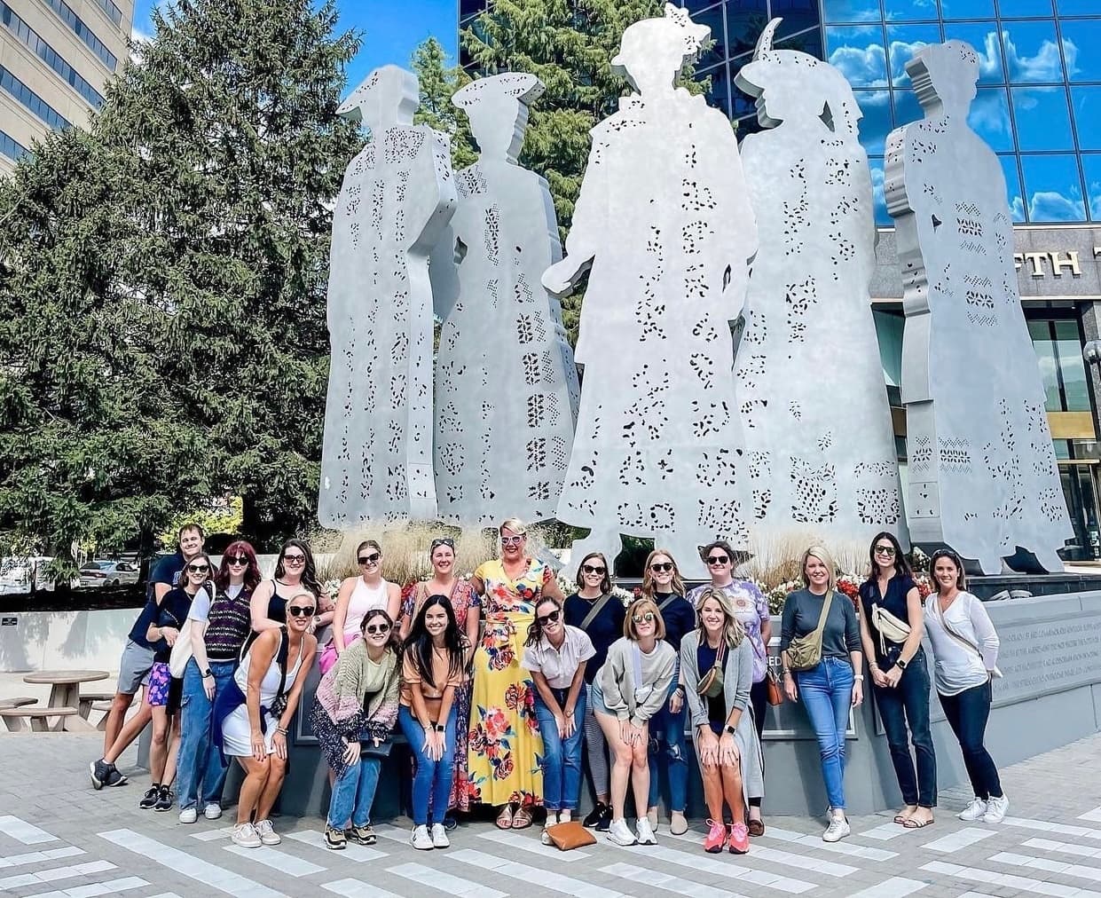 Tour group posing by large outdoor sculpture in urban plaza