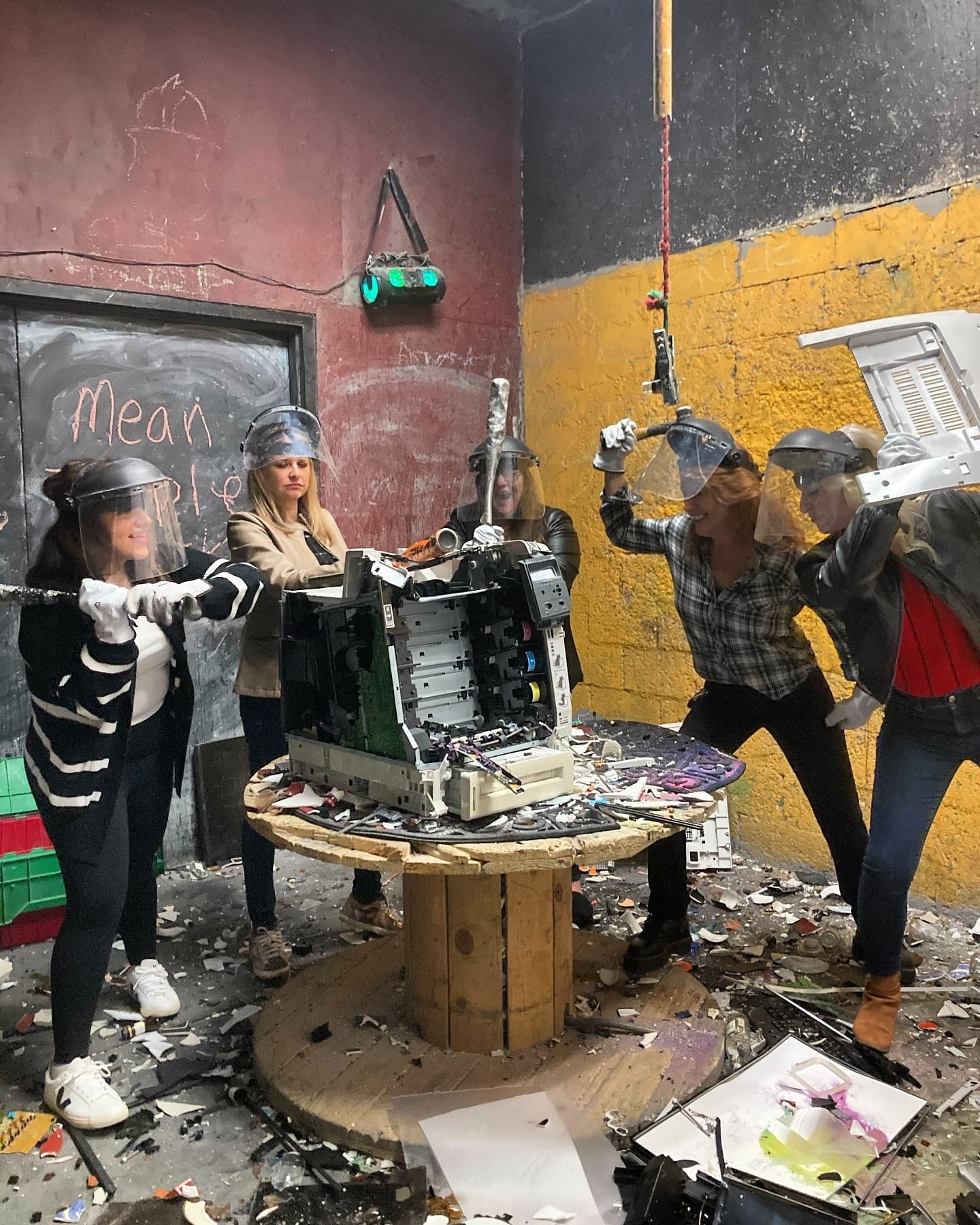 People smashing desktop computer on table inside indoor smash room