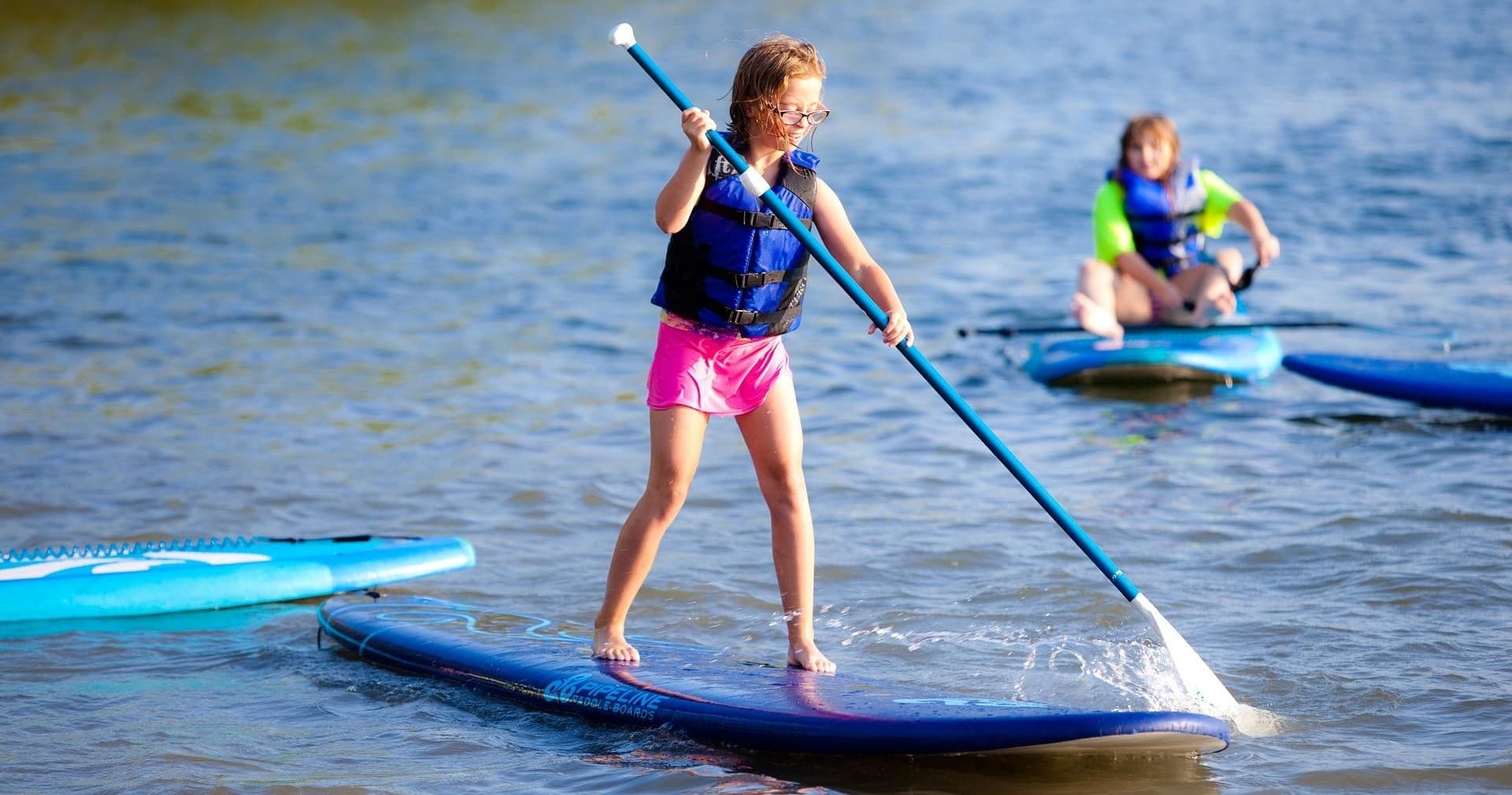 Children stand-up paddleboarding on shallow lake near shore