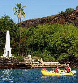Kayakers paddling near monument and lush tropical shoreline