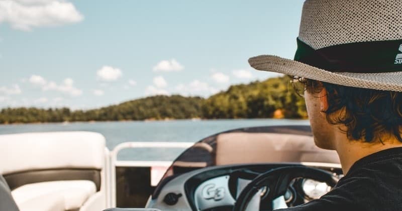 Man steering pontoon boat on sunny lake for leisure boating