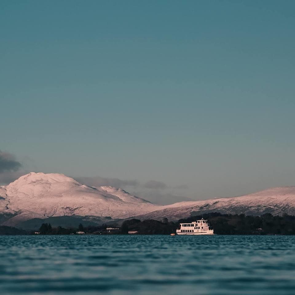 Small sightseeing ferry on alpine lake with snowy peaks