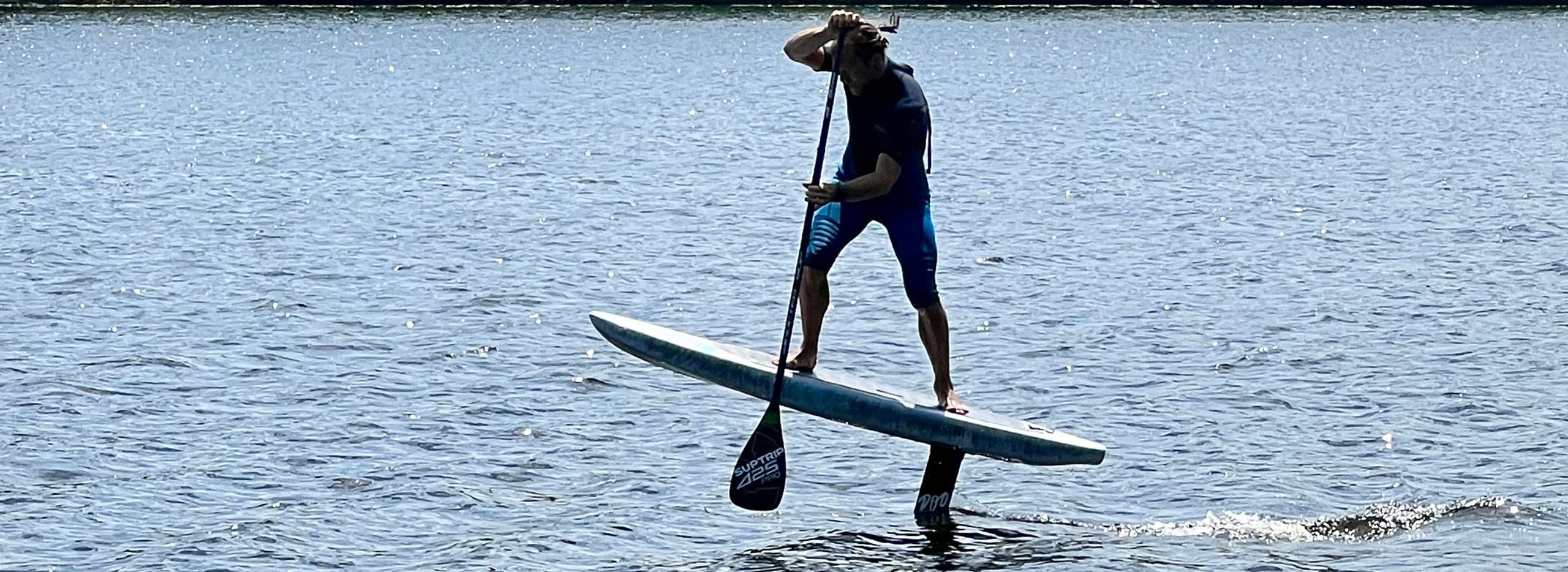 Silhouetted stand-up paddler balancing on open sea at dusk