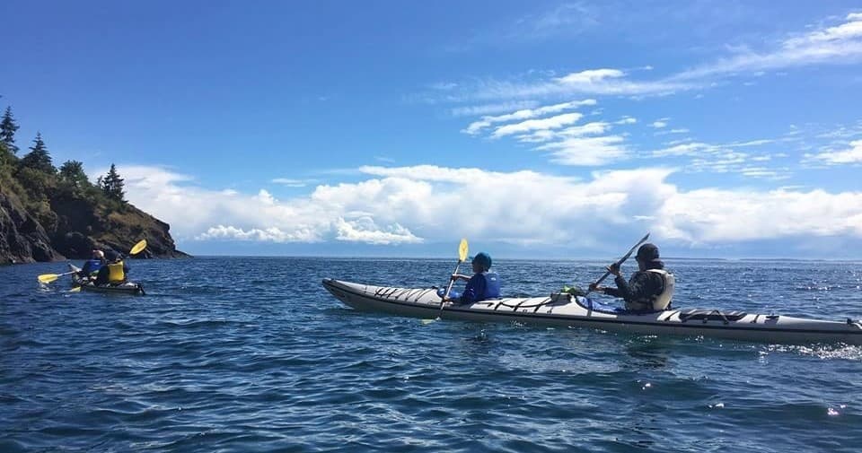 Sea kayaking past coastal cliffs under blue sky, group paddling