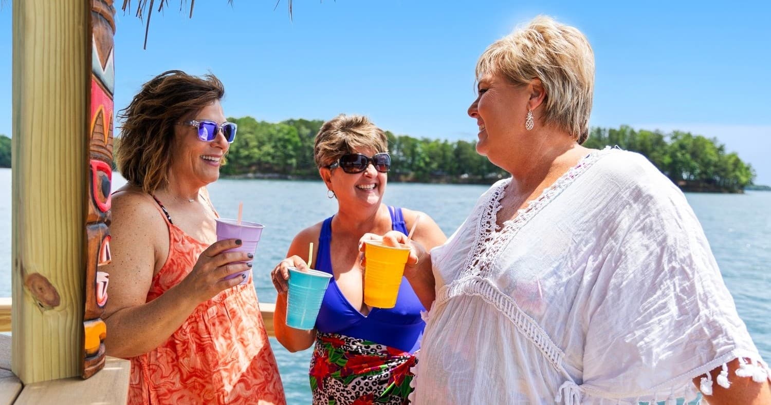 Friends sipping tropical drinks on lakeside tiki bar deck socializing