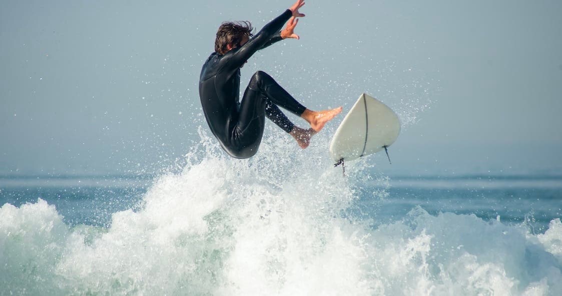 Surfer launching into the air above a breaking wave in open ocean