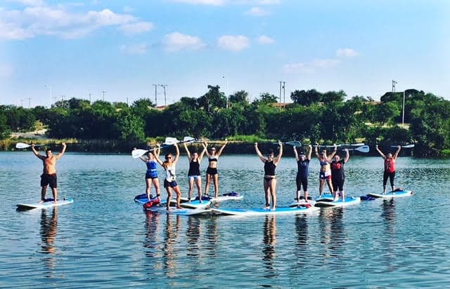 Group stand-up paddleboard yoga class on calm lake shoreline