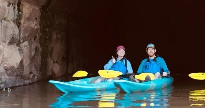 Two kayakers exploring a river cave passage at dusk