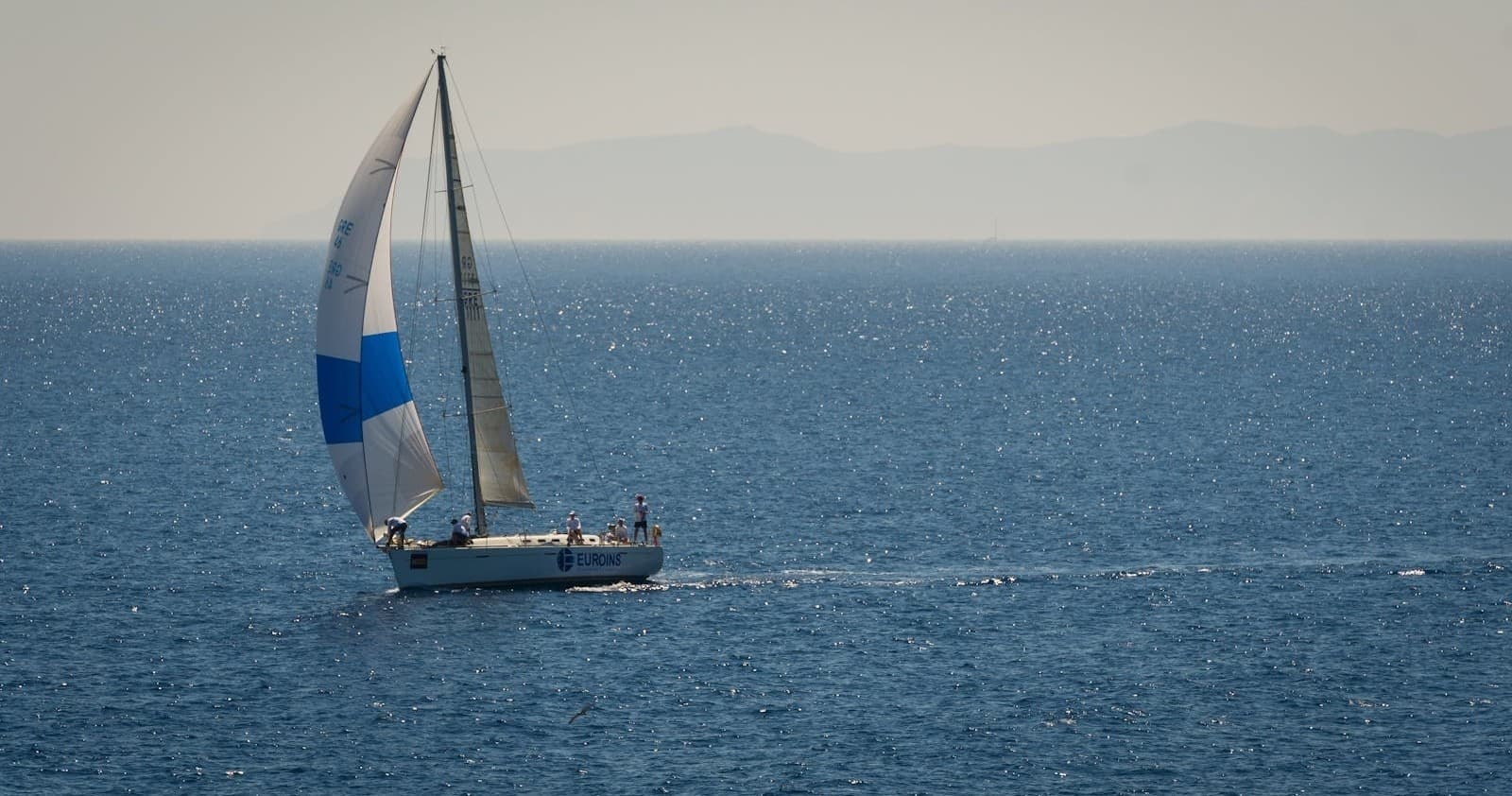 Yacht with blue spinnaker gliding on calm sea, coastal sailing